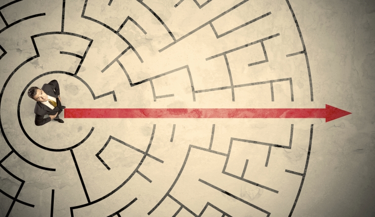 Business person standing in the middle of a circular maze with red arrow