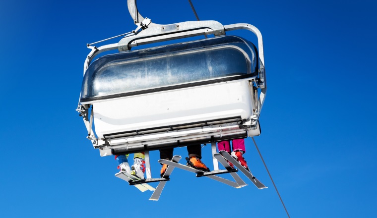 skiers in a chairlift against blue sunny sky at ski resort