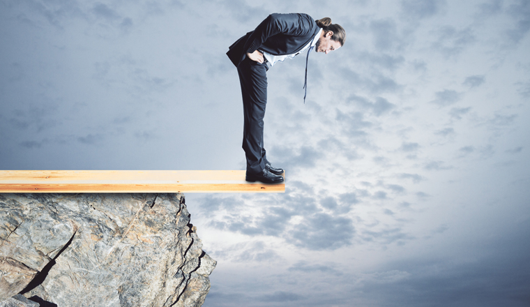 Risk and crisis concept. Young businessman looking down from cliff. Sky background 