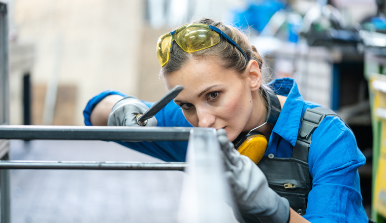 Woman metalworker checking the accuracy of her work holding steel file in her hand