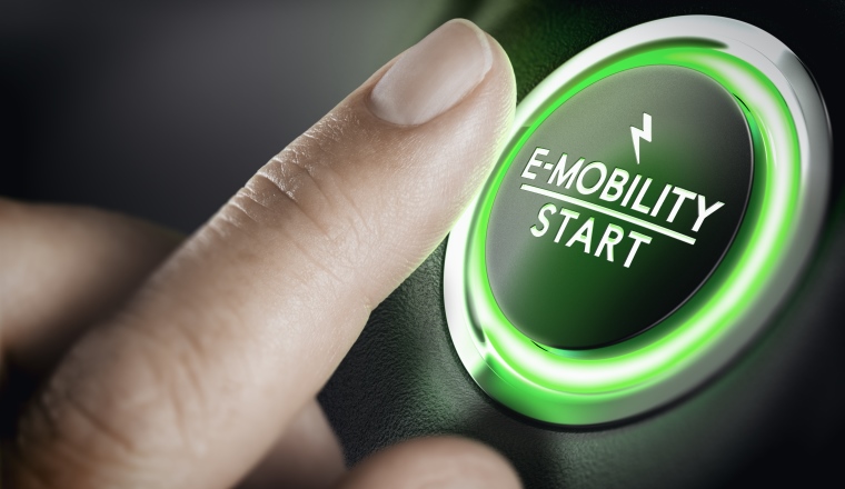 Man pushing green car button. Concept of e-mobility. Composite image between a hand photography and a 3D background.