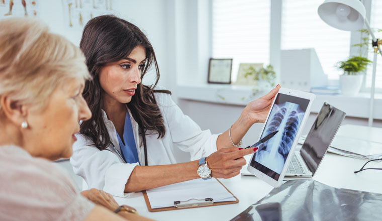 Doctor shows results to old patient x-ray of the lungs, smoking cigarettes problem. Doctor explaining lungs x-ray on Tablet PC screen to young patient. Doctor showing female patient x-ray shot in clinic office. Coronavirus chest X-ray.