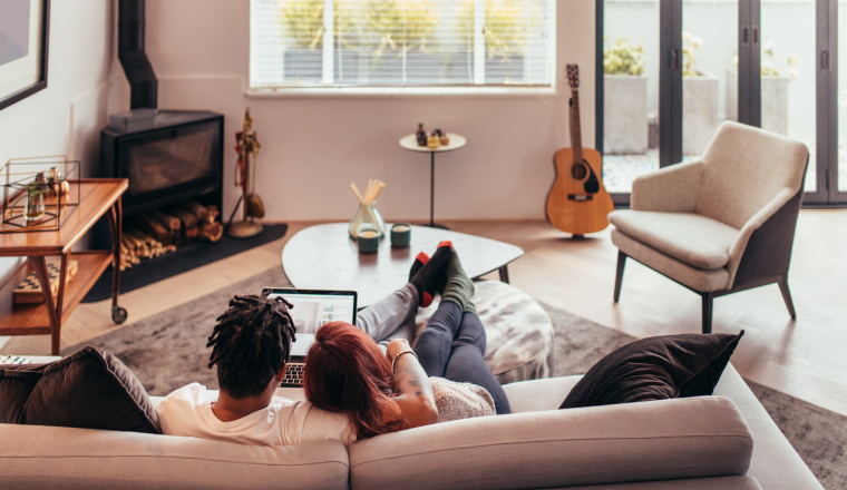 Rear view of couple relaxing on sofa and looking at laptop computer. Man and woman sitting together on couch and using laptop.