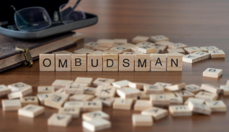 ombudsman word or concept represented by wooden letter tiles on a wooden table with glasses and a book