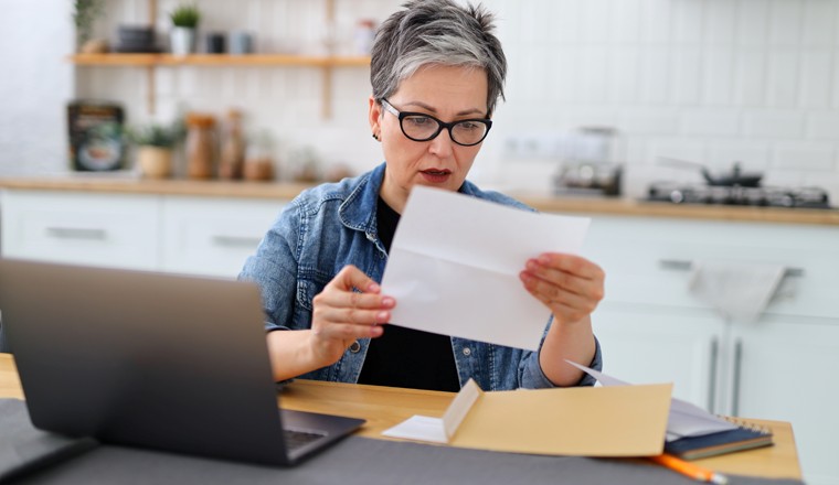 Shocked woman holding letter in home interior, high bill for payment.