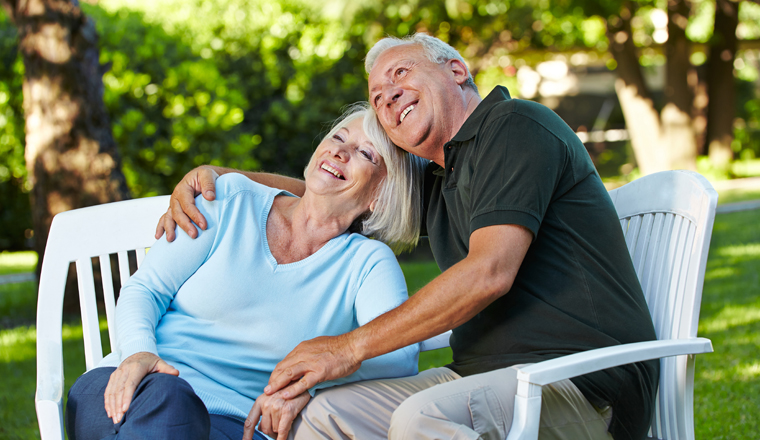 Zwei lachende Senioren sitzen glücklich im grünen Garten
