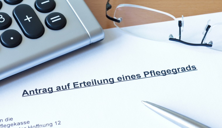 Antrag auf Erteilung eines Pflegegrads bei der Pflegekasse: Brief, Papier mit Taschenrechner, Lesebrille eines Mannes und Stift, Kuli