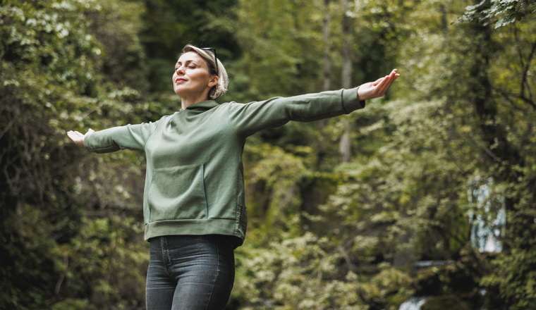 Woman with arms outstretched taking deep breath at nature and enjoying in fresh air in the mountain.