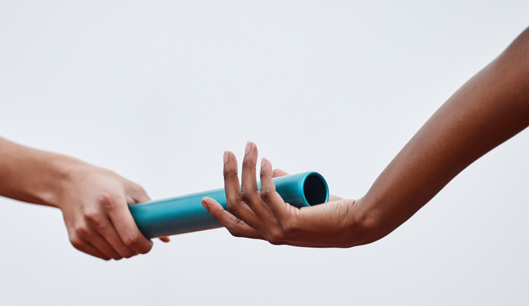 Shot of two athletes passing a baton during a relay race.