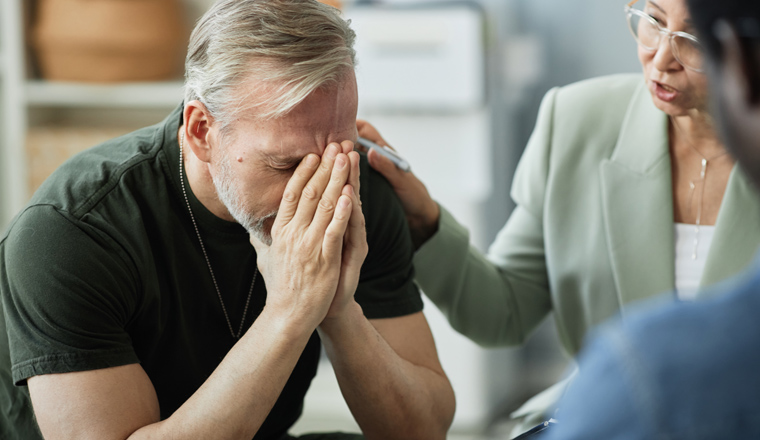 Focus on stressed grey haired man covering his face while suffering from post traumatic syndrome after coming back home after war