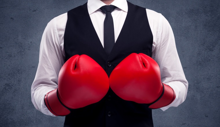A well dressed sales person standing with red boxing gloves on his hand in front of urban grey wall background concept.