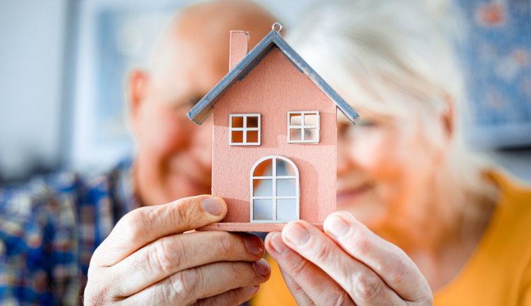 New house concept, happy senior couple holding small home model