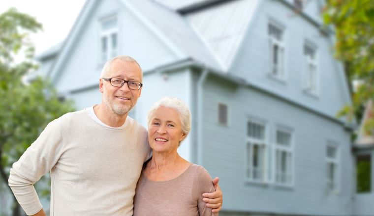 old age, accommodation and real estate concept - happy senior couple hugging over house background