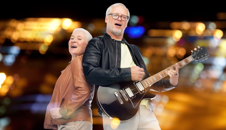 music, age and people concept - happy senior couple with electric guitar singing over night lights background