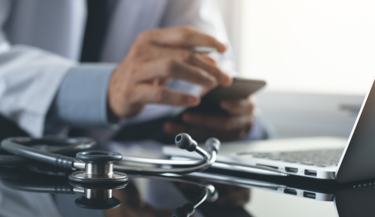 Telemedicine, Medical technology and internet concept. Doctor using mobile smart phone, working on laptop computer with stethoscope on desk, close up