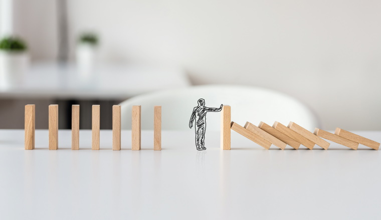 Hand drawn shape of businessman stopping domino effect in a conceptual image of solving business crisis.