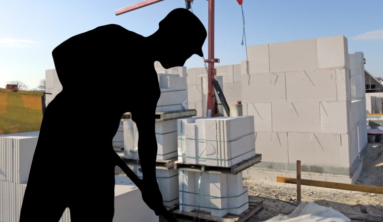 Schwarze Silhoutte eines Bauarbeiters mit Schaufel, im Hintergrund ein Rohbau