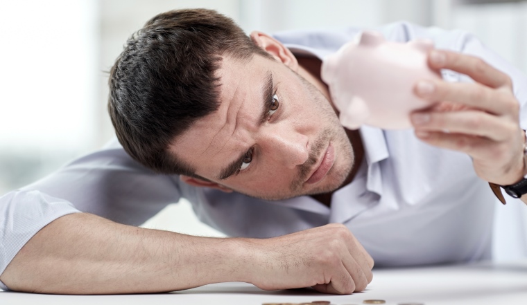 business, people, finances, crisis and money saving concept - businessman shaking piggy bank and getting coins at office
