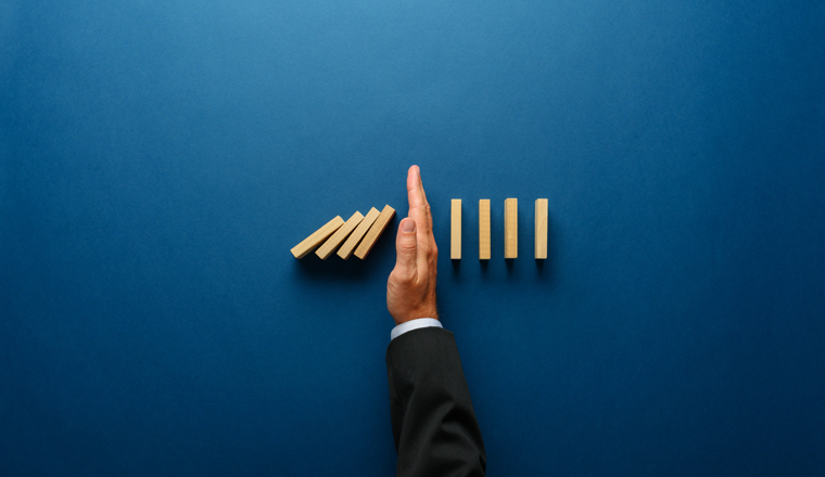 Top view  of businessman hand stopping falling dominos in a business crisis management conceptual image.