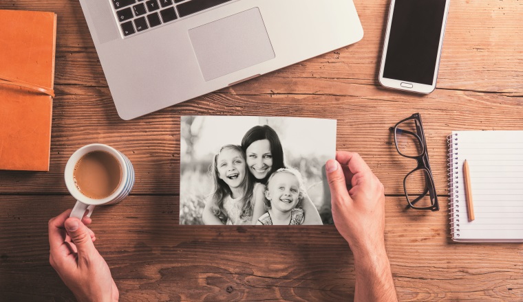 Mothers day composition. Hands of unrecognizable man holding black-and-white photo. Office desk. Studio shot on wooden background.