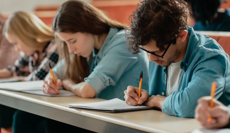 Row of Multi Ethnic Students in the Classroom Taking Exam/ Test/ Writing in Notebooks. Bright Young People Study at University.