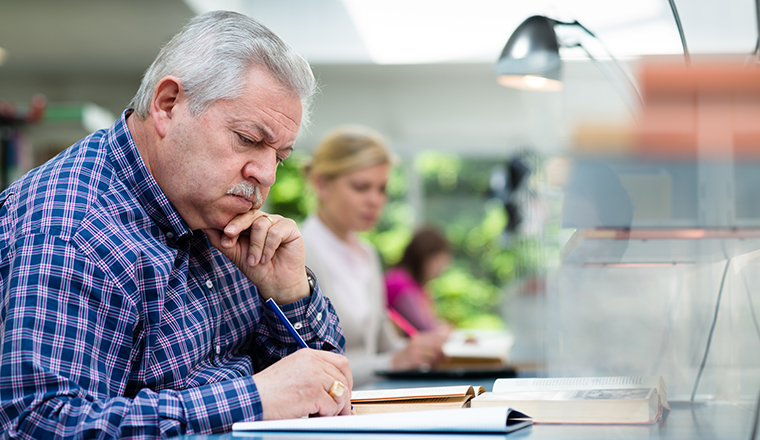 Elderly man studying with a group of young college students in library and taking notes