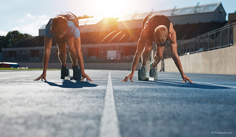 Sprinters at starting blocks ready for race . Athletes at starting position on athletics stadium race track with sun flare.