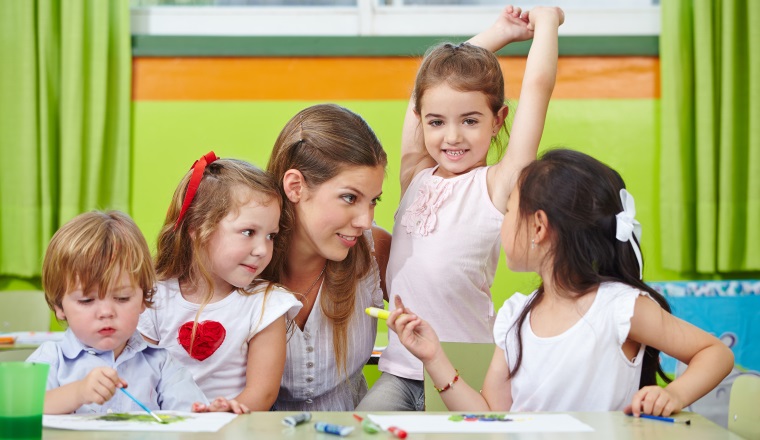 Kinder reden mit Erzieher im Kindergarten beim Malen