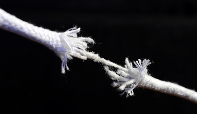 Detail of frayed ends of laundry line about to pull apart on black background stretching diagonally across the frame