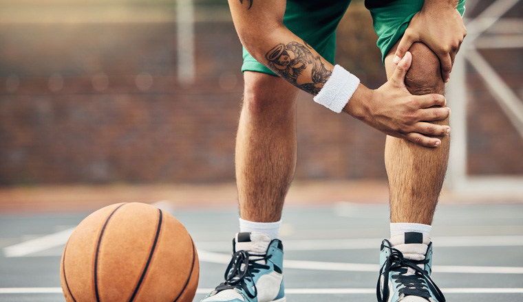 Basketball, athlete and knee injury on the basketball court during outdoor game or training. Man in with leg pain after sports accident with a broken joint, inflammation or muscle tear during match