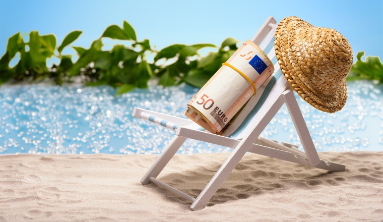Money on vacation, pack of 50 Euro bills sitting at the beach on a sun lounger in front of a blue lagoon
