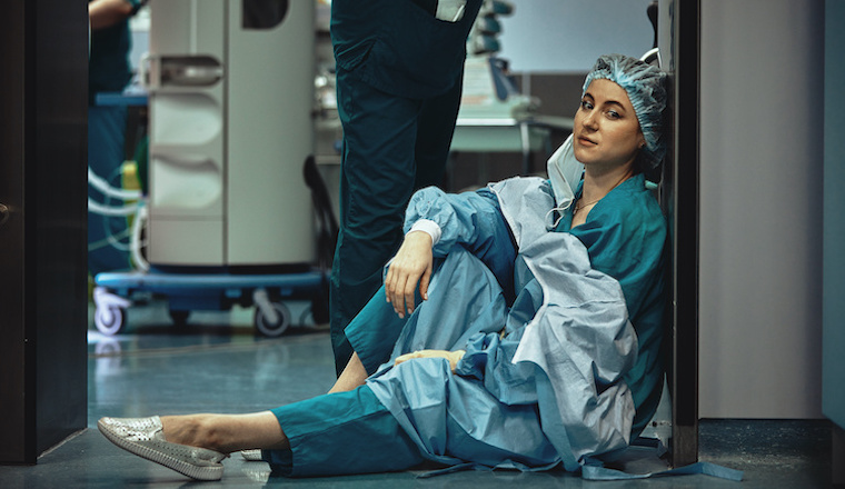 Tired doctor sitting after surgery in the hospital corridor. Great burden on doctors and medicine. Rest after work. Epidemic, lack of medical personnel, medical wards