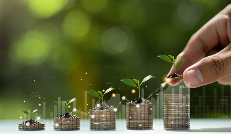 Hand putting coins on a stack with plant growing on the money with green background. Investment on bonds concept. Raising funds to fund environmentally friendly projects.Green bonds.