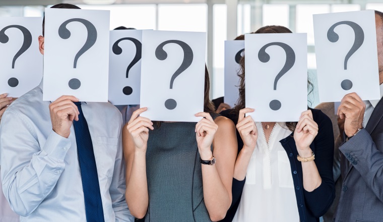 Confused business team holding a question mark sign in front of his face in office. Uncertainty and problem solving concept.