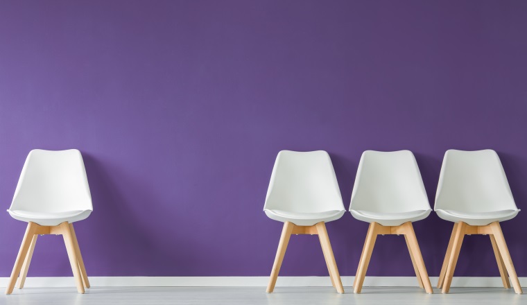 Four white chairs with wooden legs set on an empty purple wall in waiting room interior