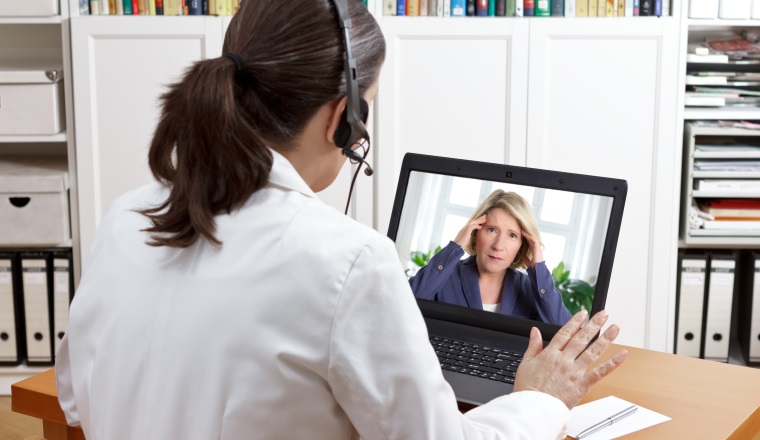 Female doctor or pharmacist in her surgery office with headset in front of her computer talking via video chat with a patient, telling her to take things easy