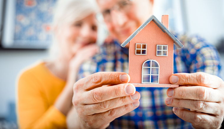 New house concept, happy senior couple holding small home model