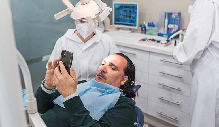 Patient using smartphone in dental office. Two female doctors preparing the procedure. concept of dental health and hygiene