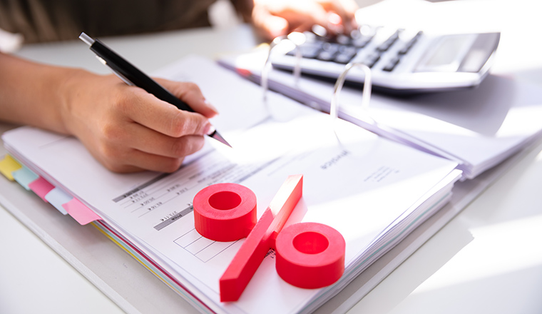 Close-up Of Red Percentage Symbol With Businessperson Calculating Bill