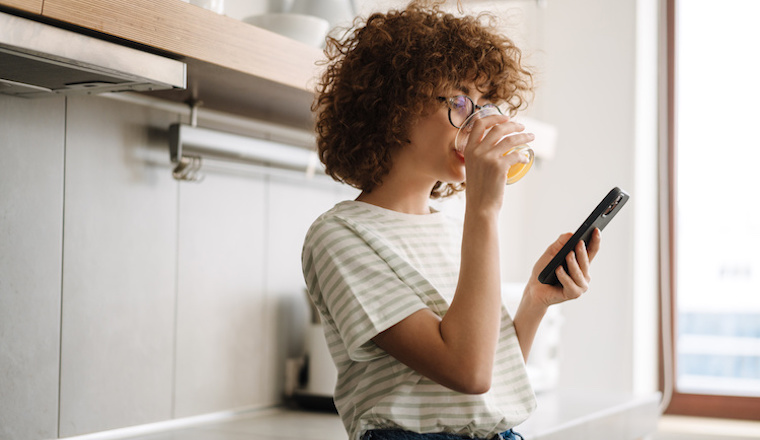 Smiling young woman on the phone in the kitchen, drinking juice
