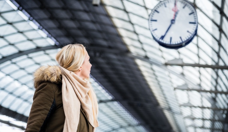 Woman looking impassionate at clock in train station as her train has a delay