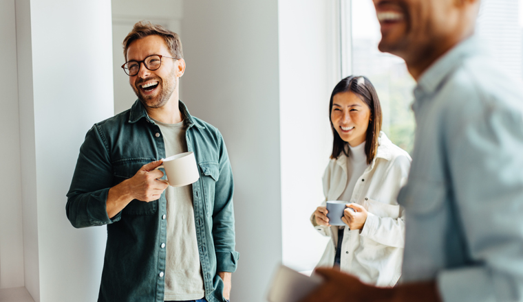 Business people laughing together during a coffee break at work. Group of young professionals standing together in an office.