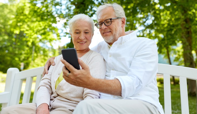 technology, relationship and old people concept - happy senior couple with smartphone taking selfie and hugging in summer