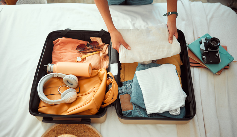 Travel packing, above and hands of a woman with clothes, holiday luggage and prepare for international summer. Suitcase, ready and person traveling with a suitcase, vacation clothing and hotel bag.
