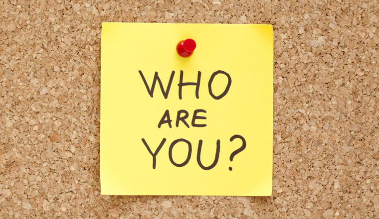 Who Are You written on an yellow sticky note pinned on a cork bulletin board.