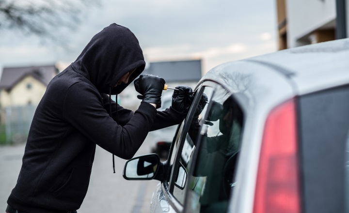 Car thief trying to break into a car with a screwdriver. Car thief, car theft.