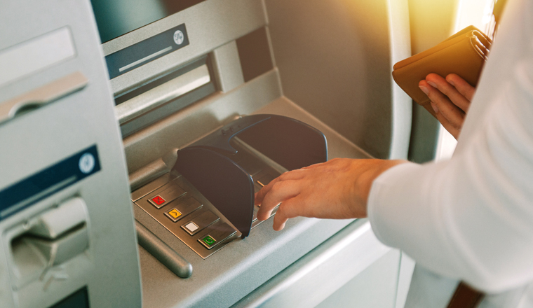 Woman using ATM holding wallet an pressing the PIN security number on the keyboard automatic teller machine 