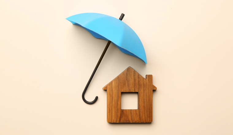 Mini umbrella and house model on beige background, flat lay
