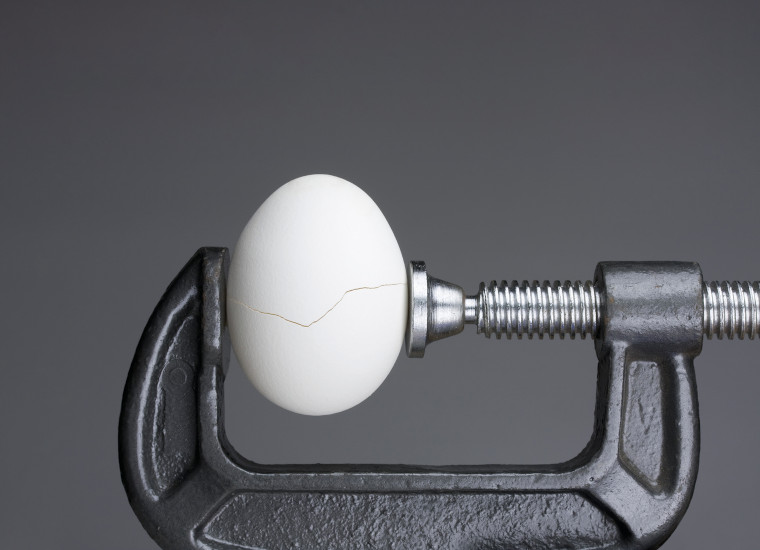 Under pressure.An egg cracking under pressure applied by squeezing clamps form the sides.