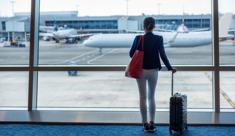 Businesswoman traveling in airport. Woman looking through the window at tarmac and planes waiting for flight. Business travel concept.